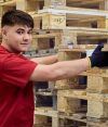 Lagerarbeiter in roter Arbeitskleidung stapelt Paletten